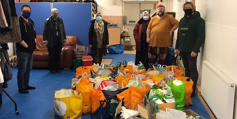 over 20 bags of food on the floor with volunteers in the background