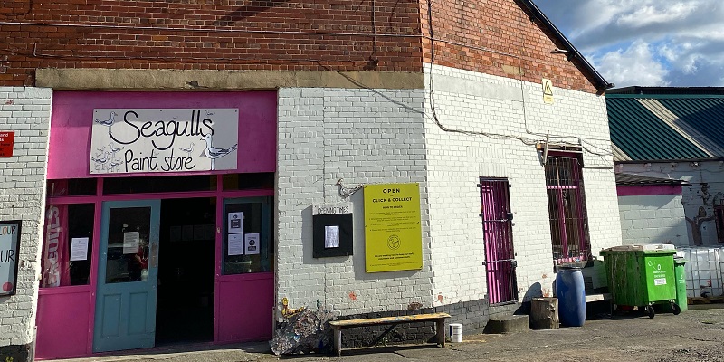 Building with white wall and pink door with seagulls sign above the door