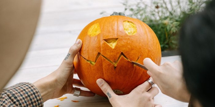 A man's hands carving a face onto a pumpkin