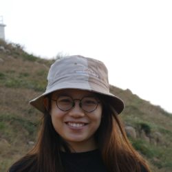 A photo of our Student Sustainability Architect Arica Ching smiling at the camera wearing a bucket hat in the countryside