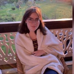 A photo of Emily Sheehy sat on a balcony, wrapped in a white blanket