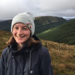 A photo of Ruth Sylvester, who is smiling on the moors in a navy jumper and white beanie.