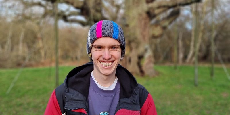 Photo of a Sam Townson stood in a field wearing a red coat and stripy hat.