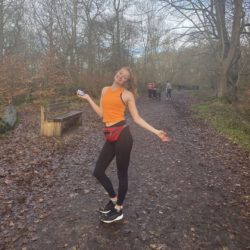 A photo of Student Sustainability Architect Jessica in an orange crop top and leggings on a countryside footpath