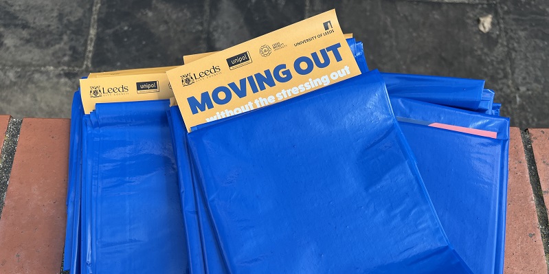 A pile of blue bags on a wall with an orange leaflet reading 'Moving Out' sticking out.