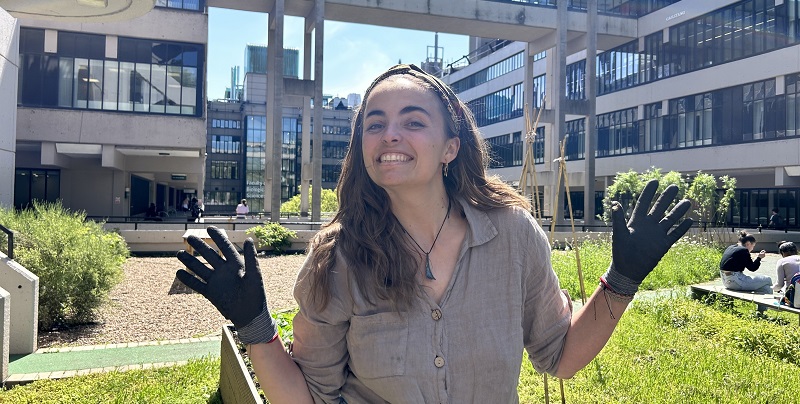 A woman with brown, shoulder length hair smiling at the camera with gardening gloves on