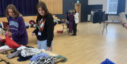 Two women stood looking at clothes on a table in the middle of a sports hall.