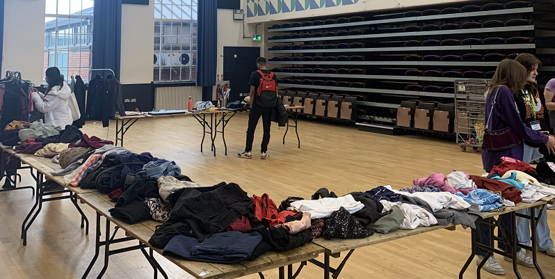 Tables with clothes on arranged in a large semi circle in a sports hall.