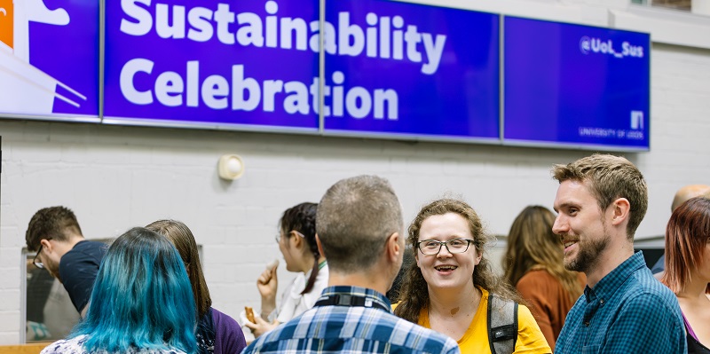 A group of people stood talking underneath a blue banner that reads 'Sustainability Celebrations'.