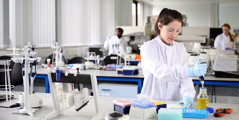 A brunette lady in a lab coat using a pipette in a lab.