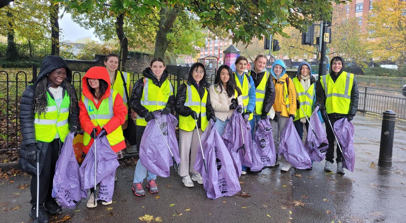 A group of students wearing high vis jackets, carrying rubbish bags and litter pickers.