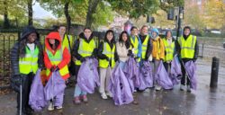 A group of students smiling, holding litter pickers and rubbish bags.