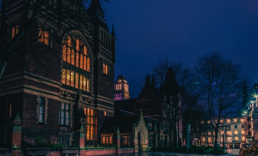 A picture of the Great Hall at the University of Leeds at night time, lit up through the windows.