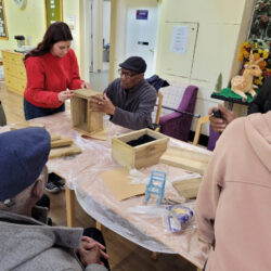 A student helps community members assemble a wooden planter.