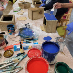On a table is various paints, brushes, and woodwork tools.