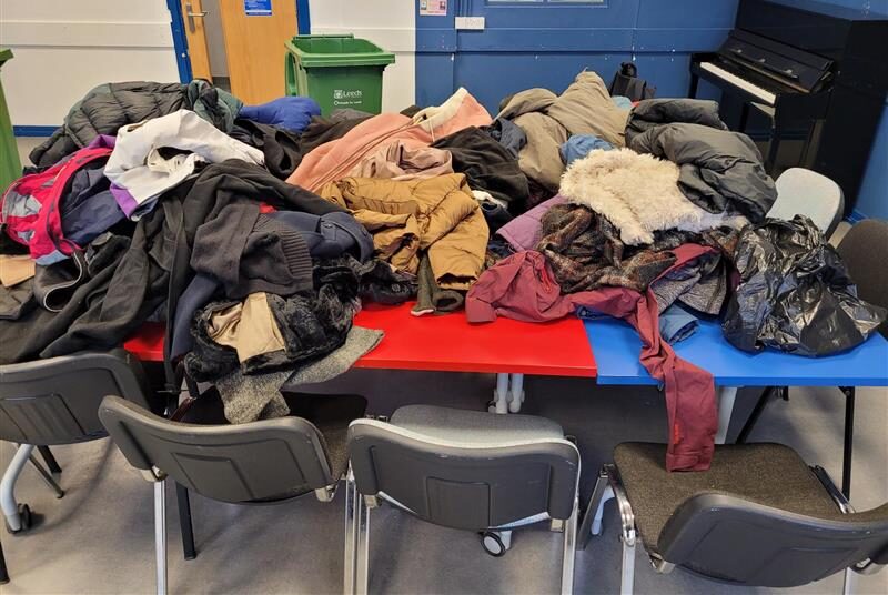 A table with a large pile of winter coats on top.