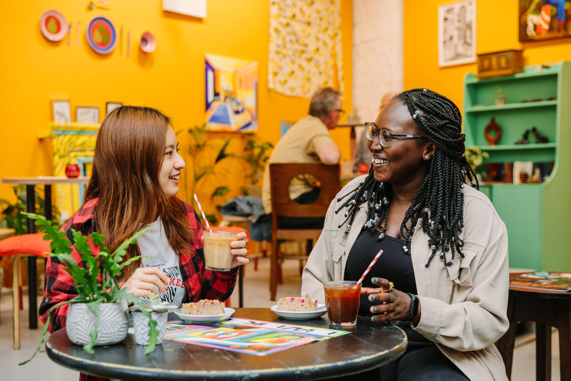 Two women are sat at a table in a brightly coloured cafe.