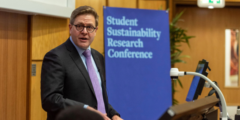Professor Jeff Grabill addressses the Student Sustainability Research Conference in 2024 at the Unviersity of Leeds. He is wearing a suit and tie and looking towards the camera. A blue banner behind him reads 'Student Sustainability Research Conference'