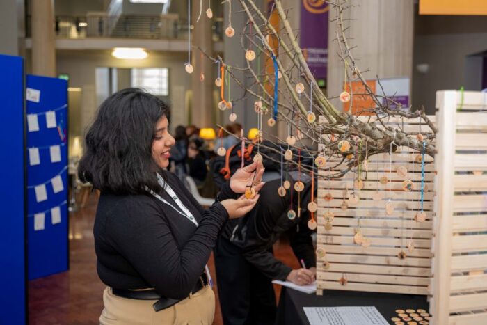 An installation piece at the conference where small tags with artwork on are hung up on a branch. A student examines one of the tag's artwork.