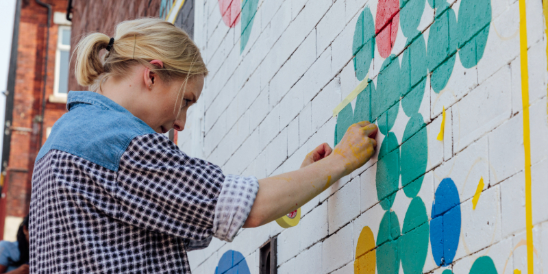 A lady painting a mural on a brick wall