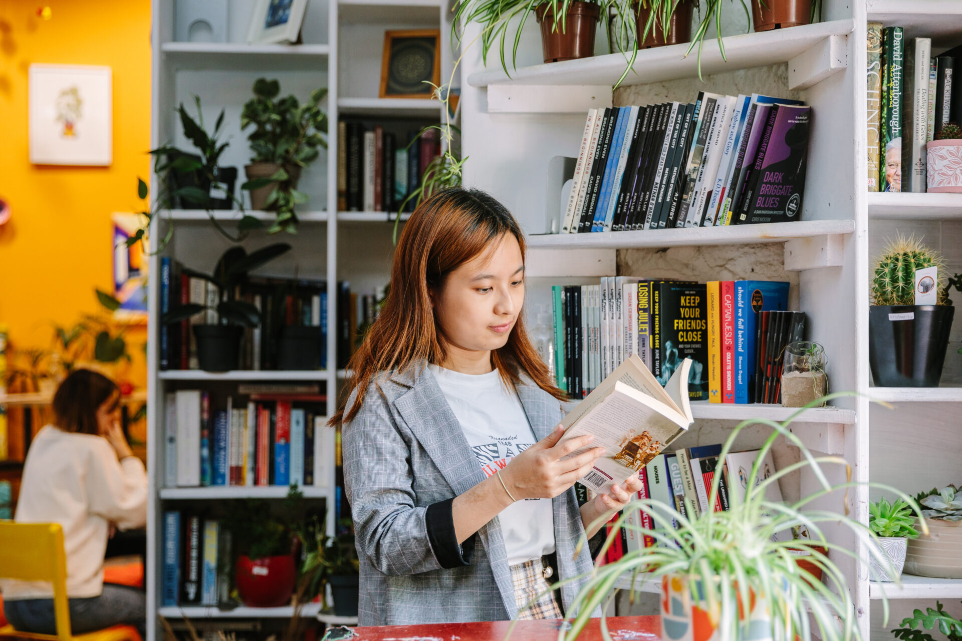 A person reading a book next to a shelf.
